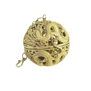May include: A gold-colored metal ornament shaped like a sphere with a dragon design. The ornament has a loop at the top for hanging and is intricately detailed.