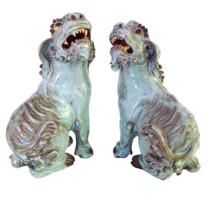 May include: A pair of green glazed ceramic foo dogs, traditional Chinese guardian lions, with intricate details and a distressed finish.