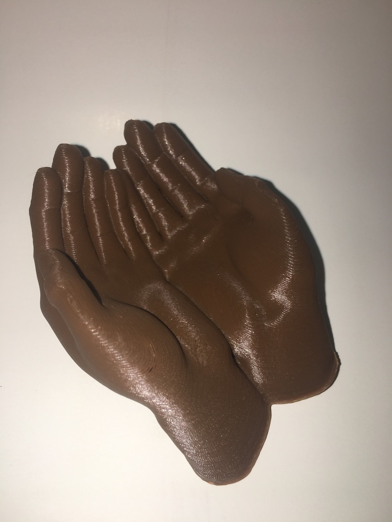 K&ouml;nnte beinhalten: Eine braune 3D-gedruckte Skulptur von zwei zusammen gefalteten H&auml;nden.