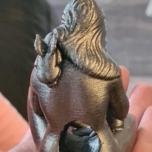 K&ouml;nnte beinhalten: Eine silberfarbene 3D-gedruckte Figur einer Frau, die mit gekreuzten Beinen sitzt und ihre Arme um sich selbst geschlungen hat. Die Figur hat eine detaillierte, strukturierte Oberfl&auml;che.