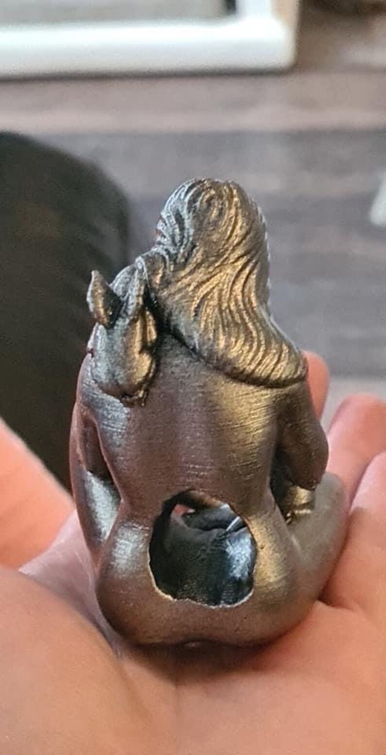 K&ouml;nnte beinhalten: Eine silberfarbene 3D-gedruckte Figur einer Frau, die mit gekreuzten Beinen sitzt und ihre Arme um sich selbst geschlungen hat. Die Figur hat eine detaillierte, strukturierte Oberfl&auml;che.