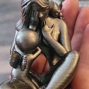 K&ouml;nnte beinhalten: Eine silberfarbene Metallskulptur einer Mutter und eines Kindes. Die Mutter h&auml;lt das Kind in ihren Armen, und das Kind hat Fl&uuml;gel. Die Skulptur ist detailliert und realistisch.