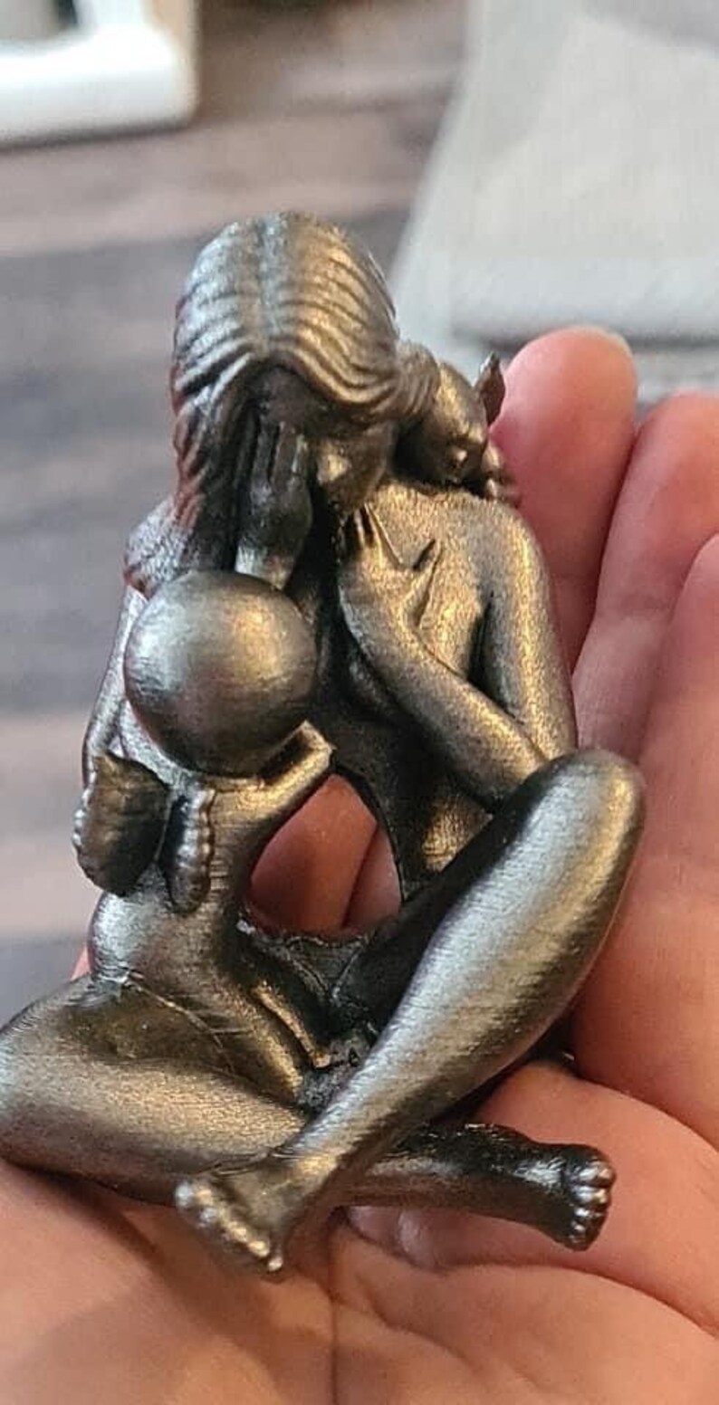 K&ouml;nnte beinhalten: Eine silberfarbene Metallskulptur einer Mutter und eines Kindes. Die Mutter h&auml;lt das Kind in ihren Armen, und das Kind hat Fl&uuml;gel. Die Skulptur ist detailliert und realistisch.