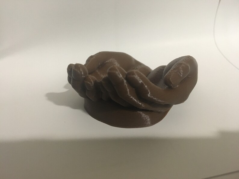 K&ouml;nnte beinhalten: Eine 3D-gedruckte Skulptur aus zwei ineinander gelegten H&auml;nden, aus braunem Kunststoff.