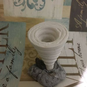 May include: White ceramic tornado sculpture with a swirling design. The base is a textured gray rock.