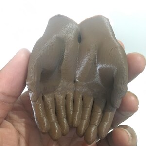 K&ouml;nnte beinhalten: Eine 3D-gedruckte Skulptur von zwei ineinander verschlungenen H&auml;nden. Die Skulptur ist aus braunem Kunststoff und hat eine glatte, gl&auml;nzende Oberfl&auml;che.