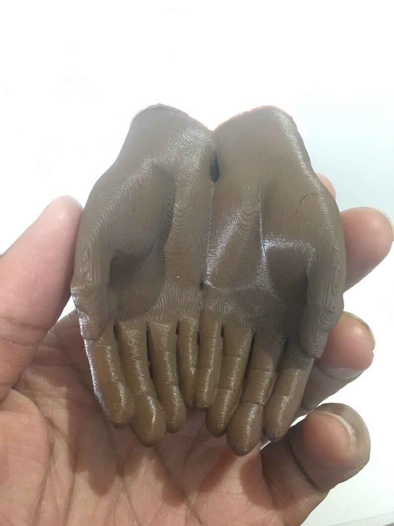K&ouml;nnte beinhalten: Eine 3D-gedruckte Skulptur von zwei ineinander verschlungenen H&auml;nden. Die Skulptur ist aus braunem Kunststoff und hat eine glatte, gl&auml;nzende Oberfl&auml;che.