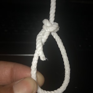 Puede incluir: Una cuerda blanca atada en un nudo simple, formando un bucle.