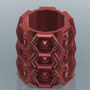 Può includere: Un contenitore cilindrico rosso con un motivo geometrico e una parte superiore liscia e arrotondata. Il contenitore è realizzato in un materiale solido e presenta un motivo ripetitivo di forme esagonali.