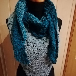 Könnte beinhalten: Ein türkisfarbenes und hellblaues Häkeltuch mit einem gewellten Rand. Das Tuch ist über eine schwarze Schaufensterpuppe gelegt.