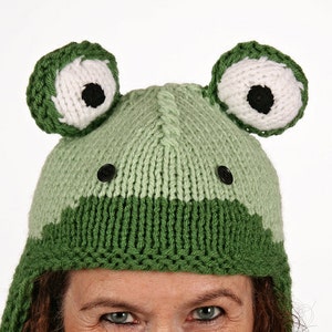 Könnte beinhalten: Grüne gestrickte Frosch-Mütze mit weißen Augen und schwarzen Pupillen. Die Mütze hat einen Farbverlauf von Grün zu Hellgrün.