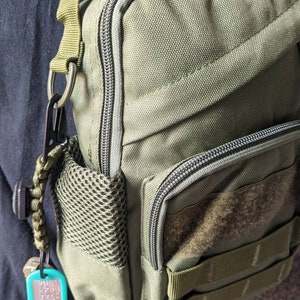 Peut inclure: Un sac à bandoulière tactique vert avec une poche zippée, une poche en filet et une sangle velcro. Le sac a un anneau en D et un porte-clés attaché.