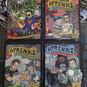 May include: Four comic book covers featuring a tattoo artist apprentice. The covers are black with colorful illustrations. The titles are "Aprendiz: The True Saga of Any Tattoo Apprentice" and the book numbers are "Book One", "Book Two", "Book Three", and "Book Four".