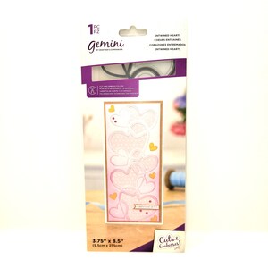 May include: A pink and white die-cut card with a design of intertwined hearts. The card is 3.75 inches by 8.5 inches. The die-cut is for use with a die-cutting machine.