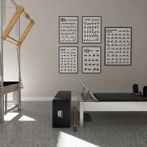 May include: A Pilates studio setup featuring a reformer, a Cadillac, and exercise charts. The reformer has a black mat and a white frame. The Cadillac has wooden and metal components. Exercise charts are in black frames.