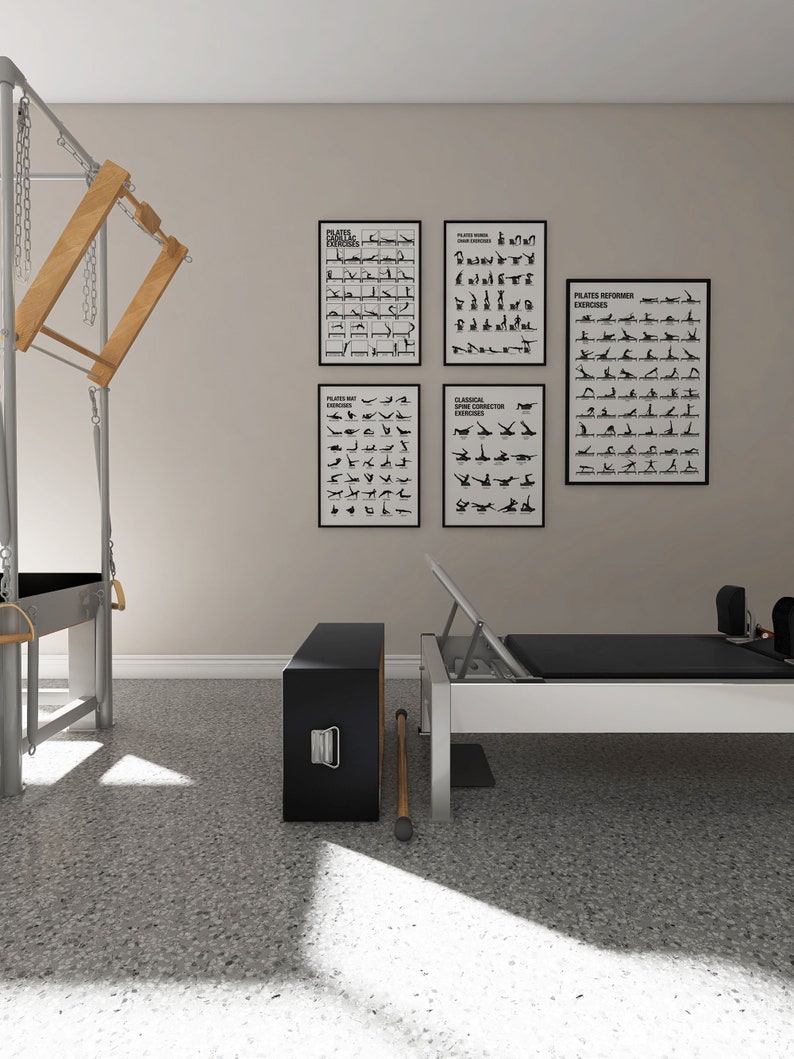 May include: A Pilates studio setup featuring a reformer, a Cadillac, and exercise charts. The reformer has a black mat and a white frame. The Cadillac has wooden and metal components. Exercise charts are in black frames.