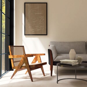 May include: A mid-century modern living room with a light brown wooden chair with a woven cane seat and back, a gray sofa, a black round coffee table with books and a vase, and a framed abstract art print on the wall.