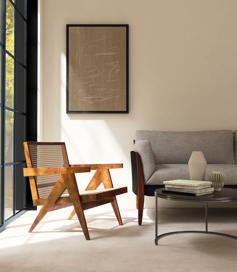 May include: A mid-century modern living room with a light brown wooden chair with a woven cane seat and back, a gray sofa, a black round coffee table with books and a vase, and a framed abstract art print on the wall.