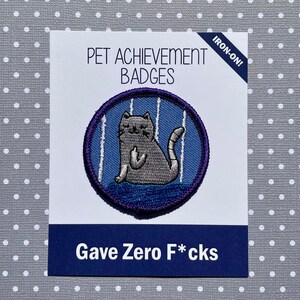 May include: Iron-on patch featuring a cartoon cat giving the middle finger. The patch is purple and blue with white stripes. The text below the patch reads "Gave Zero F*cks" and "Pet Achievement Badges".