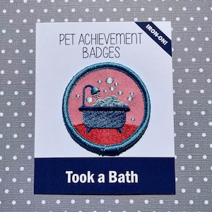 Puede incluir: Insignia de logro para mascotas para planchar con una imagen bordada de una bañera con burbujas en azul, rosa y rojo. El texto "Took a Bath" está impreso en la insignia.