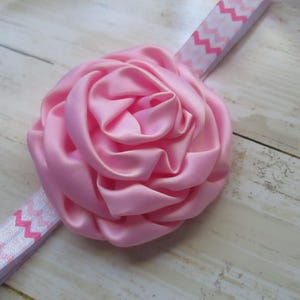 May include: A pink satin flower headband with a white and pink chevron pattern.