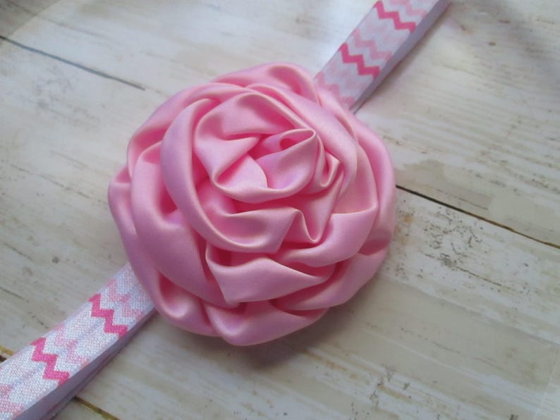 May include: A pink satin flower headband with a white and pink chevron pattern.