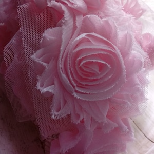 May include: A pink fabric flower bouquet with a layered, ruffled design. The bouquet is made of soft, delicate fabric and has a romantic, feminine aesthetic.