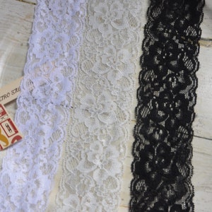 May include: Three strips of lace in white, cream, and black. The lace features a floral design and a scalloped edge. A small tag with the text "Retro Studio" and retro illustrations is visible.