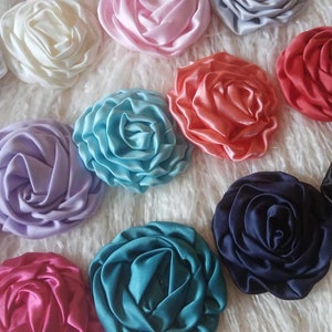 May include: Assortment of 12 handmade satin fabric rosettes in various colors, including pink, blue, purple, red, white, and black.
