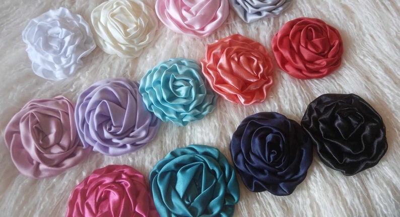 May include: Assortment of 12 handmade satin fabric rosettes in various colors, including pink, blue, purple, red, white, and black.