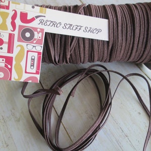 Può includere: Un rotolo di cordoncino elastico marrone con un'etichetta che recita "Retro Stuff Shop".