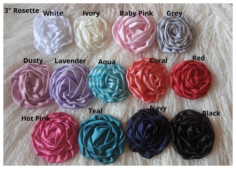 May include: A collection of 12 3-inch satin rosettes in various colors, including white, ivory, baby pink, grey, dusty rose, lavender, aqua, coral, red, hot pink, teal, navy, and black.