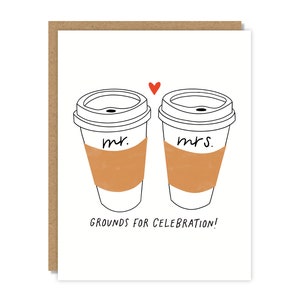 May include: A white card with a black line drawing of two coffee cups. The cups have the words "Mr." and "Mrs." written on them. A red heart is drawn above the cups. The text "GROUNDS FOR CELEBRATION!" is written below the cups.