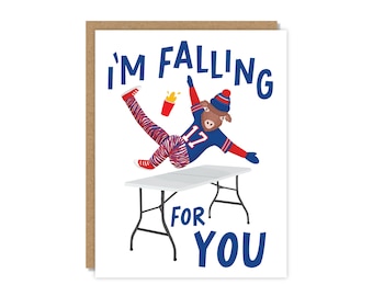 May include: Greeting card with a cartoon buffalo wearing a football uniform, falling off a table. Text reads "I'M FALLING FOR YOU" in blue. The card has a brown border.