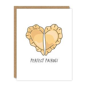 May include: A greeting card with a white background and a brown border. The card features a heart-shaped illustration of two pierogies, with the text "PERFECT PAIROGI" below the illustration.