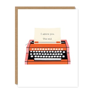 May include: Greeting card featuring a retro orange typewriter with a white keyboard and a sheet of paper. The paper reads "I adore you. The end." The card is set against a white background and framed by a brown border.