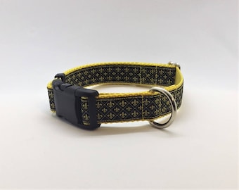 Könnte beinhalten: Schwarzes und gelbes Hundehalsband mit einem goldenen Fleur-de-lis-Muster. Das Halsband hat eine schwarze Kunststoffschnalle und einen silbernen D-Ring.
