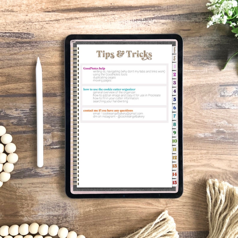 May include: A digital tablet with a pink and white background displaying a list of tips and tricks for using the GoodNotes app. The list includes information on writing, navigating, using tools, duplicating pages, moving pages, and using a cookie cutter organizer. The tablet is on a wooden surface.