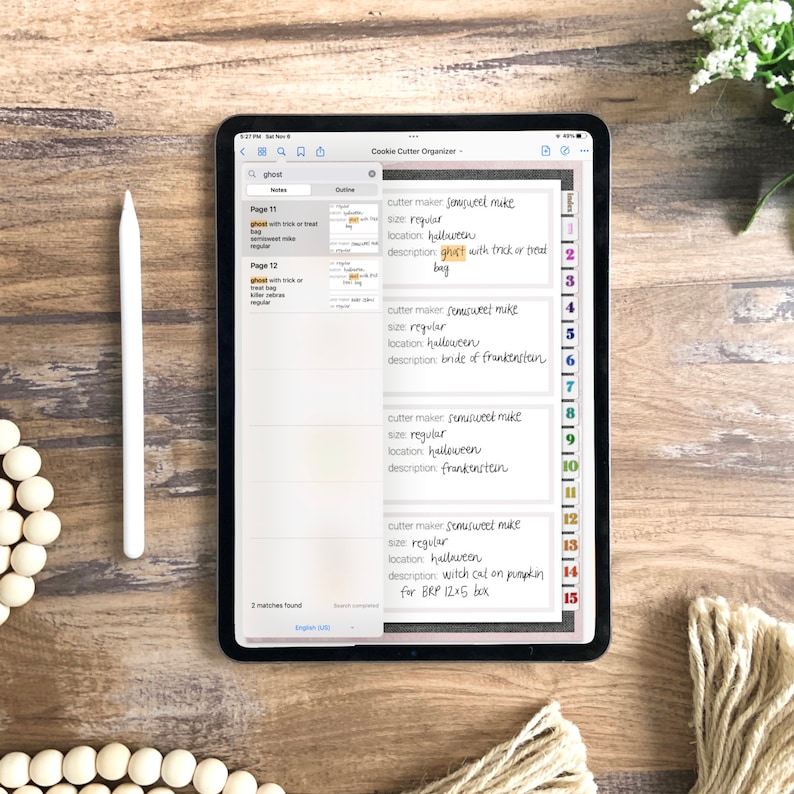 May include: A digital tablet screen displaying a list of cookie cutters for Halloween. The list includes the cutter maker, size, location, and description for each cutter. The list is organized by page number. The tablet is on a wooden surface.