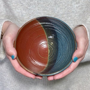 May include: A handmade ceramic bowl with a red and blue glaze. The bowl has a unique swirl pattern and is perfect for serving snacks or desserts.