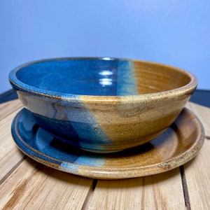 May include: A blue and brown ceramic bowl with a matching plate. The bowl and plate have a glazed finish and are handmade.