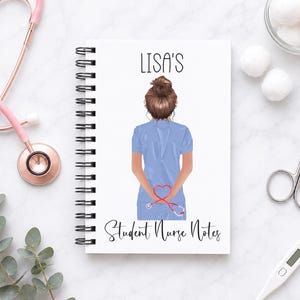 May include: A spiral-bound notebook with a white cover featuring an illustration of a person with a brown bun hairstyle wearing light blue scrubs. The text reads "LISA'S" and "Student Nurse Notes" with a red stethoscope shaped like a heart.
