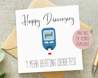 May include: A white card with the words "Happy Diaversary" and "1 Year Beating Diabetes!". It features a blue blood glucose meter with "good" on the screen. The card is on a brown envelope, with a gold pen visible.