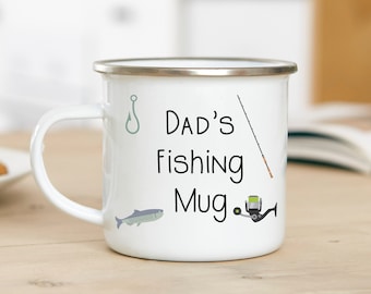 May include: White enamel mug with a black and white design that says "Dad's Fishing Mug." The mug has a silver rim and a black handle. There are illustrations of a fishing hook, a fishing rod, a fish, and a fishing reel.