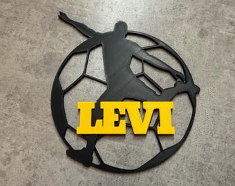 May include: Black silhouette of a football player kicking a ball with the name "LEVI" in yellow letters on a black football.