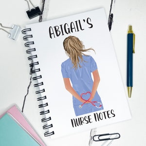 May include: A white spiral bound notebook with the text "ABIGAIL'S NURSE NOTES" printed on the cover. The cover also features a cartoon illustration of a woman in a blue medical uniform with a stethoscope around her neck. The stethoscope is shaped like a heart.