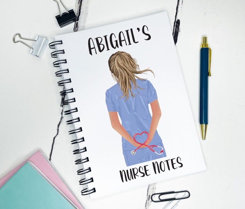 May include: A white spiral bound notebook with the text "ABIGAIL'S NURSE NOTES" printed on the cover. The cover also features a cartoon illustration of a woman in a blue medical uniform with a stethoscope around her neck. The stethoscope is shaped like a heart.
