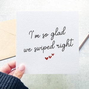 May include: A white card with the text "I'm so glad we swiped right" in black cursive writing. There are three small red hearts below the text.