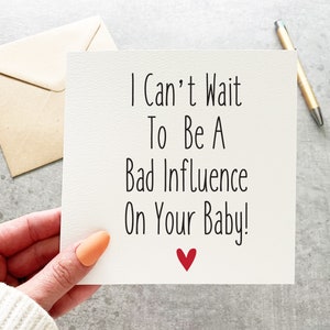 May include: A white card with black text that reads "I Can't Wait To Be A Bad Influence On Your Baby!" with a red heart at the bottom.