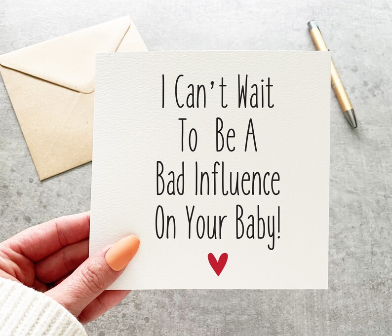 May include: A white card with black text that reads "I Can't Wait To Be A Bad Influence On Your Baby!" with a red heart at the bottom.